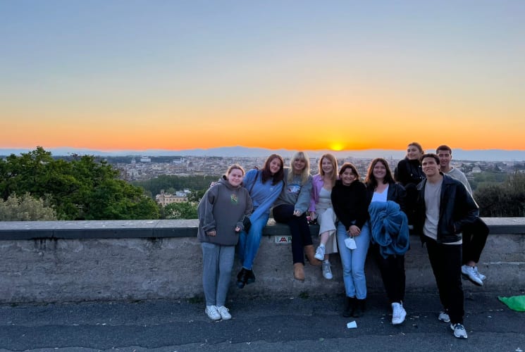 A group of students in front of a view of a sunset.